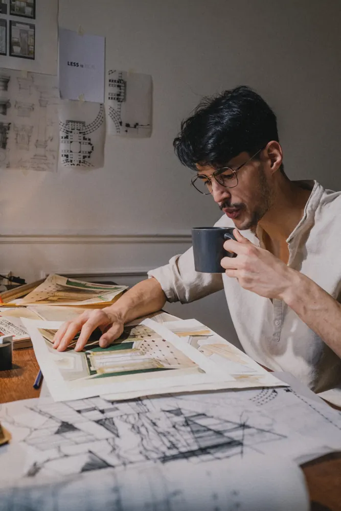 Arquitecto con una taza en la mano frente a planos y bocetos