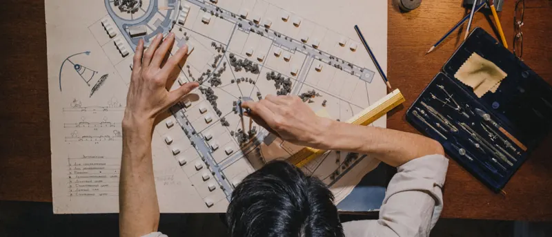 Vista cenital de unas manos trabajando sobre un plano con instrumentos de dibujo